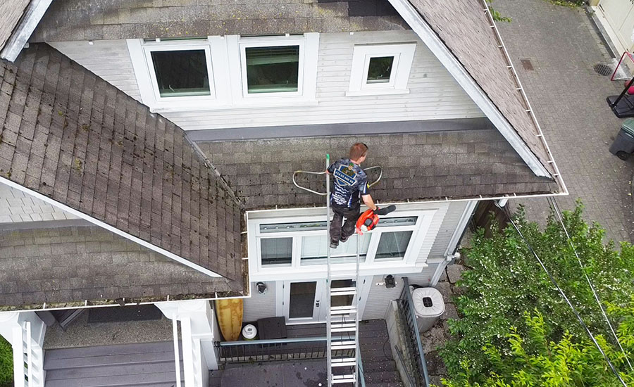 a clean squad employee cleaning gutters while on a ladder. the photo is taken from above with a drone.